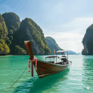 เรือหางยาวไทยในอ่าวที่สวยงามของภูเก็ต เรือหางยาวไทยจอดลอยลำบนน้ำทะเลสีฟ้าคราม แสดงตัวเลือกทัวร์ภูเก็ตที่พบบ่อย